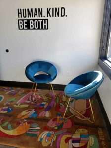 Thought Distillery lounge area with teal velvet chairs, colorful rug and wall decal that says human kind be both