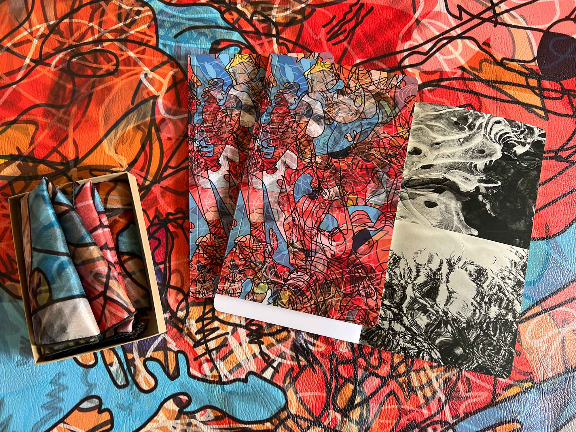 Photograph of custom printed vegan leather, custom printed scarf and custom printed journal with a red, orange, yellow, and blue pattern with squiggly black lines